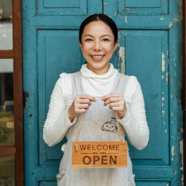 Ethnic female cafe owner showing WELCOME WE ARE OPEN inscription