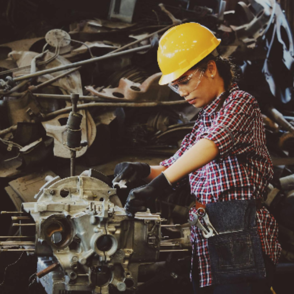 Woman Wears Yellow Hard Hat Holding Vehicle Part