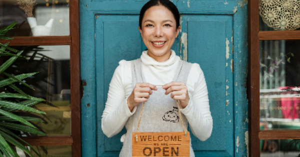 Ethnic female cafe owner showing WELCOME WE ARE OPEN inscription