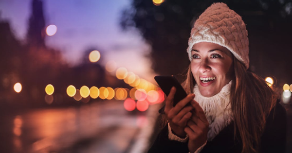 Cheerful woman recording voice message on smartphone in street