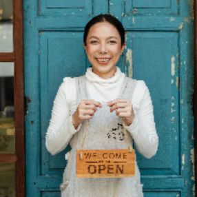 Ethnic female cafe owner showing WELCOME WE ARE OPEN inscription